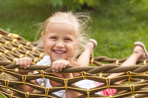 Happy Child Lying in Hammock. Cute Smiling Little Girl rides in Hammock in Nature looking at camera. Pleasant summer leisure